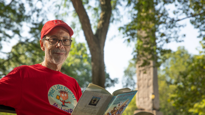 Dan Gutman sitting on a bench holding his new book